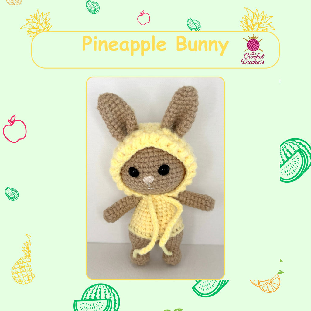 A crocheted bunny doll wearing a yellow hood and matching yellow dress, centered on a pale mint background with decorative fruit illustrations and the text 'Pineapple Bunny' and 'The Crochet Duchess'.