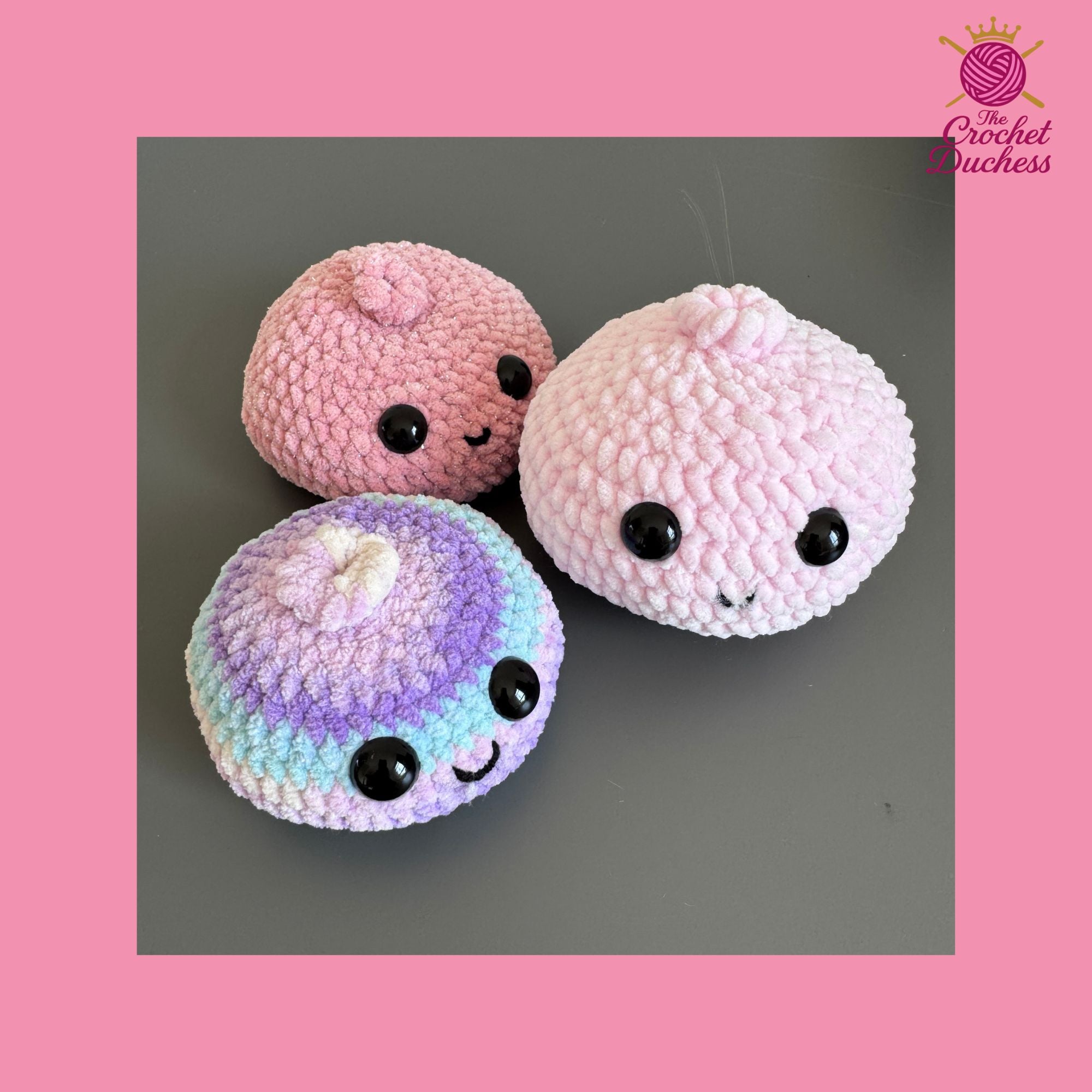 Three cute crocheted amigurumi dumpling toys with kawaii faces are displayed on a dark gray surface, set against a pink background with 'The Crochet Duchess' logo in the top right corner.